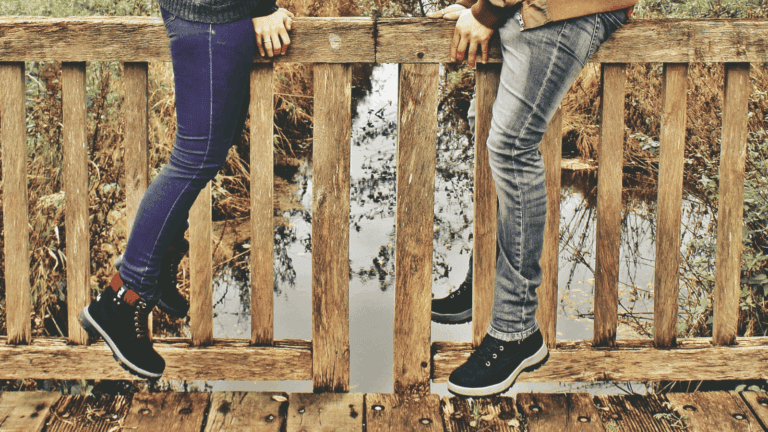 Zwei Personen auf einer Holzbrücke. Geländer markiert feste Grenze, Abstand hält Nähe geordnet, Präsenz wirkt ruhig