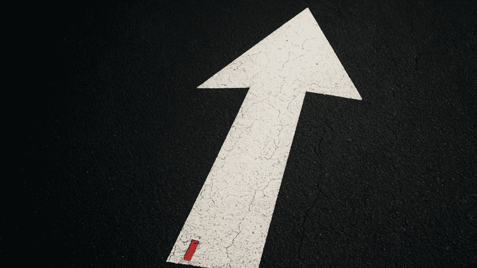 Weißer Richtungspfeil auf dunklem Asphalt steht für Fokus setzen und Innere Haltung in Beziehung im Alltag anwenden